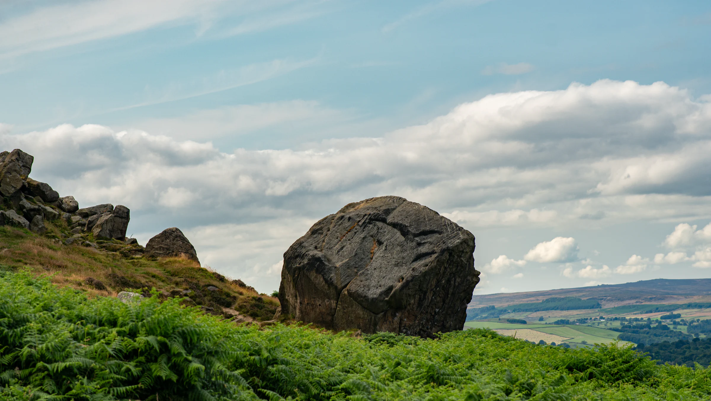 The Calf boulder sitting below the gritstone crags of the Cow and Calf on Ilkley Moor