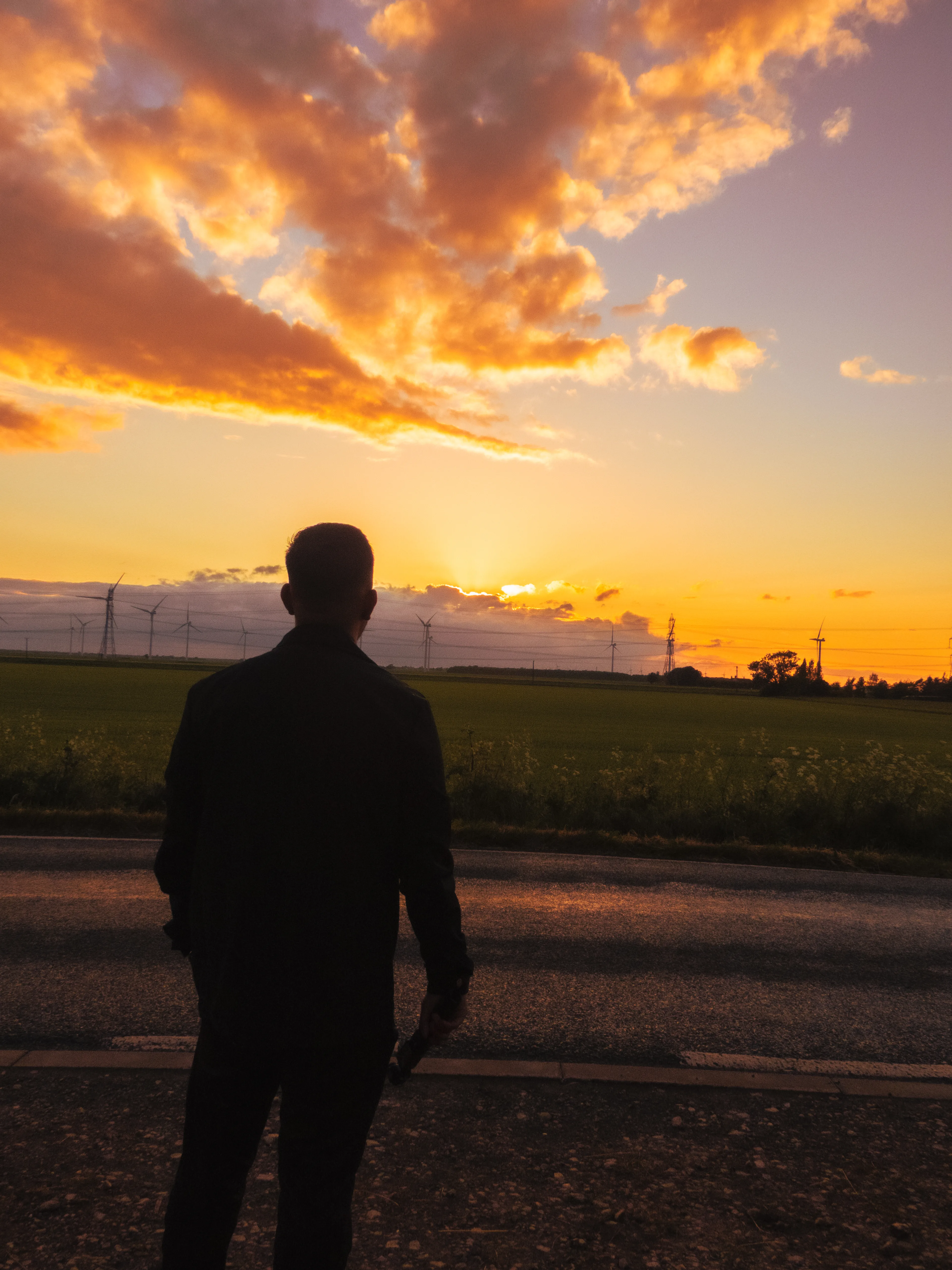 A person standing in silhouette beneath a vivid orange sunrise, looking across an open field