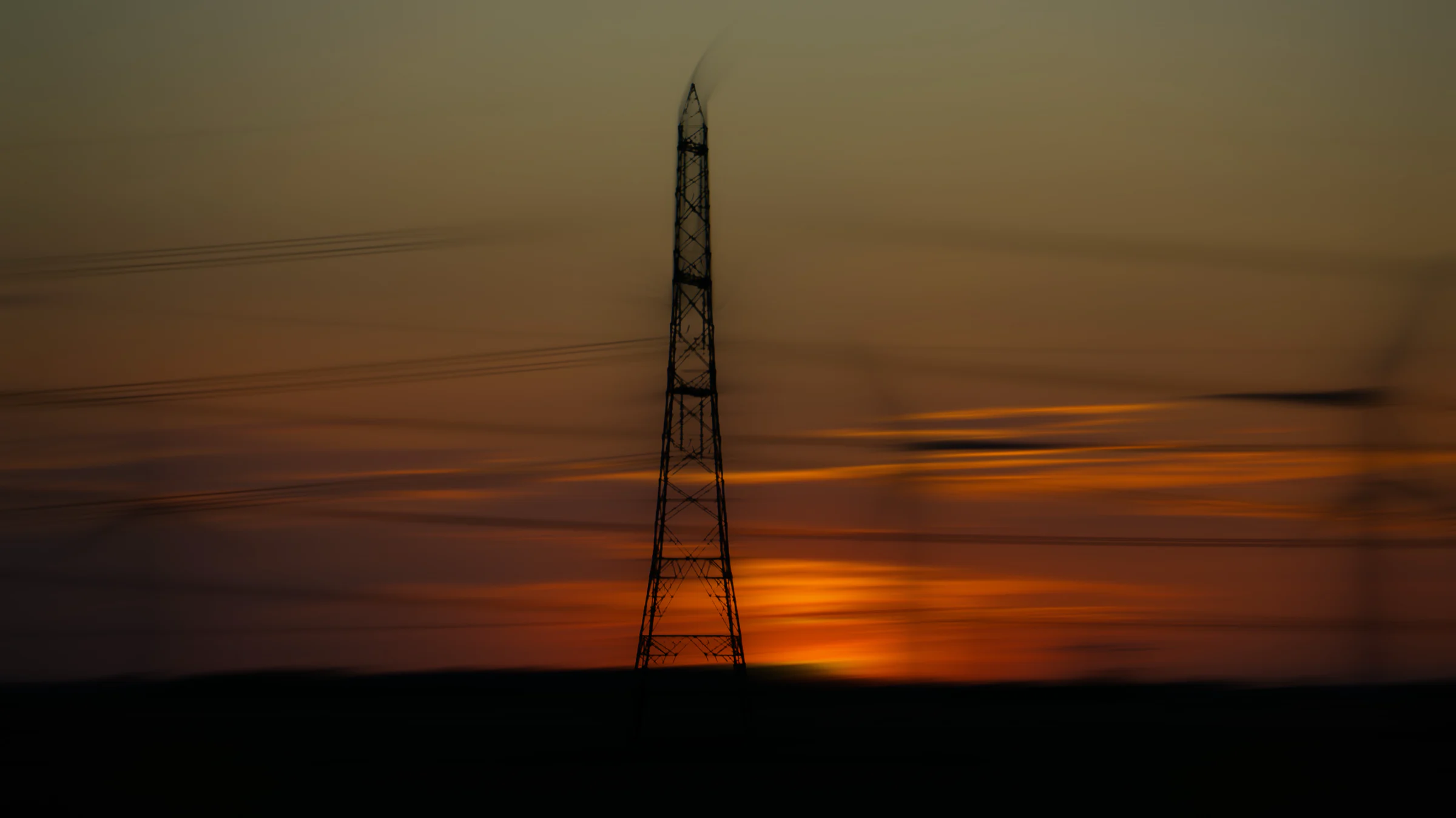 A pylon silhouetted against an orange evening sky