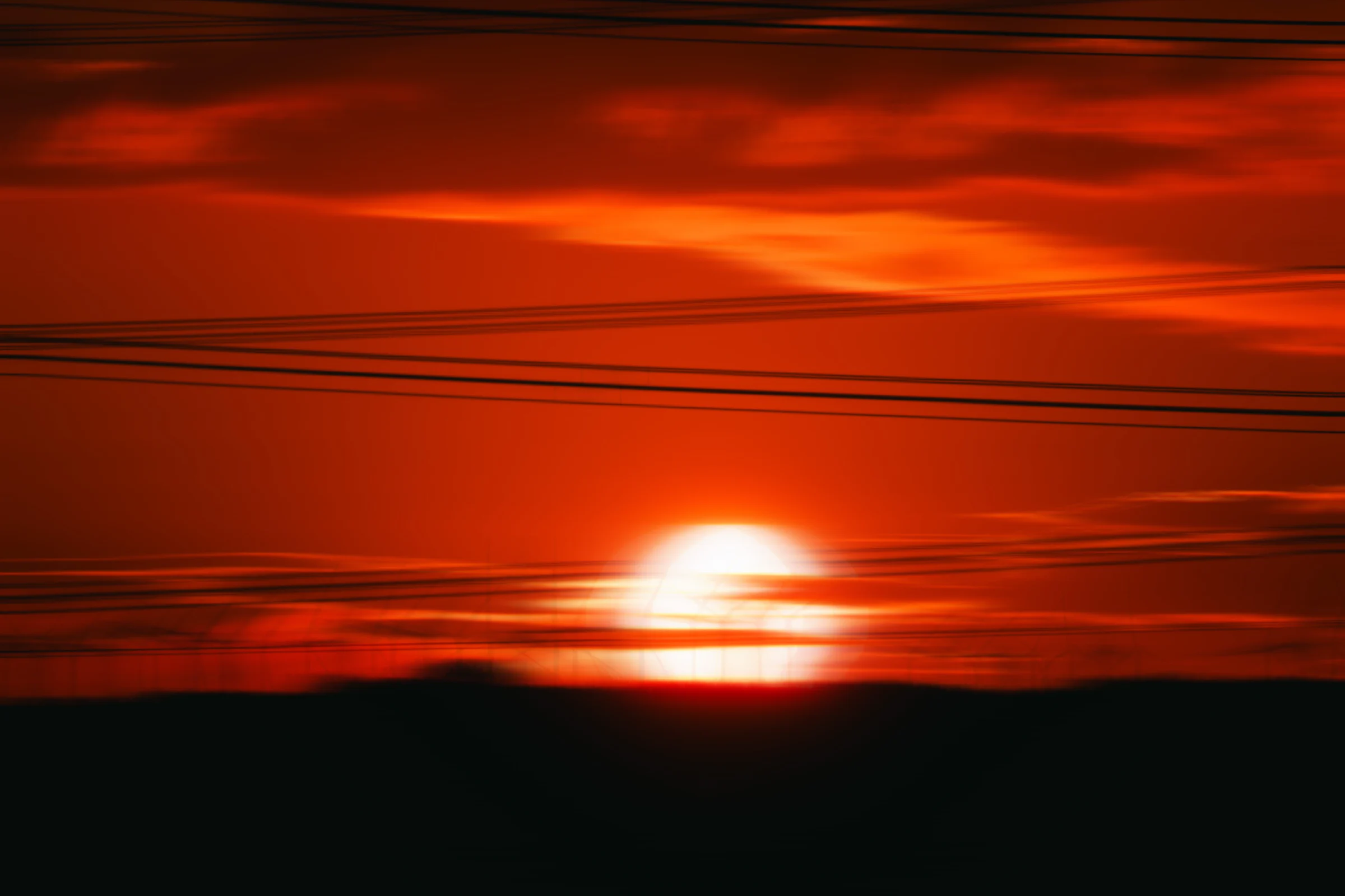 The red disc of the sun behind a tangle of power lines
