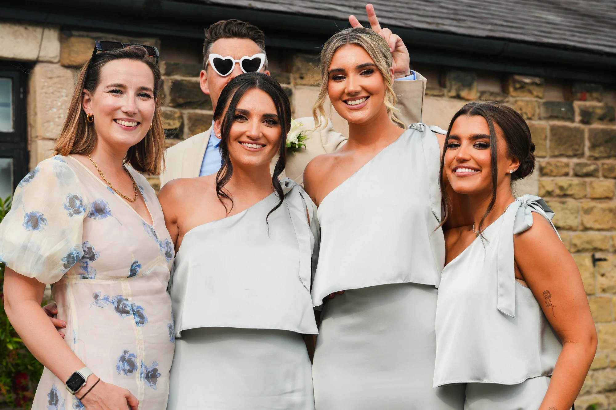 Bridesmaids in sage satin dresses laughing with friends outside the stone barn